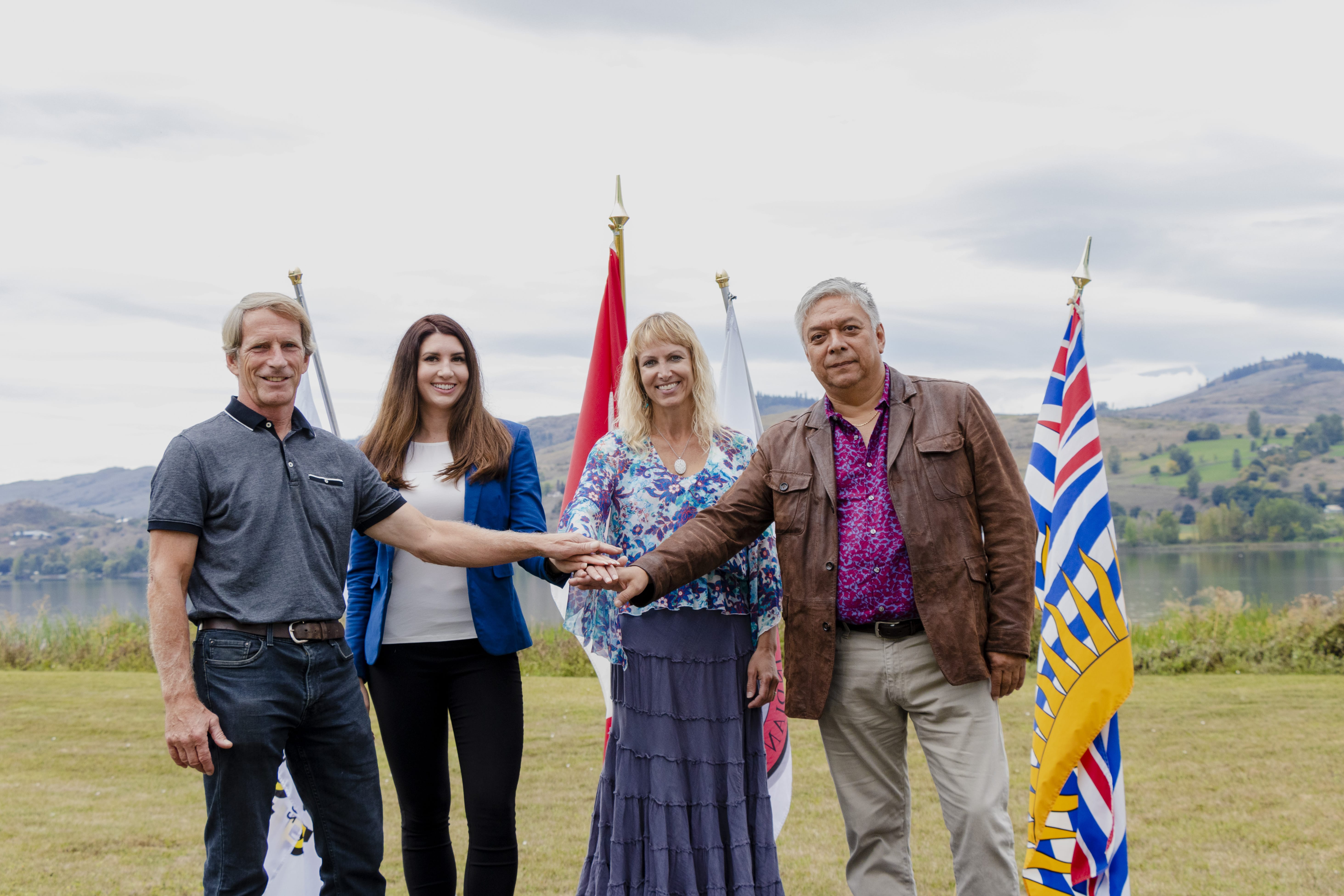Image of 4 people shaking hands with flags and mountains in the background